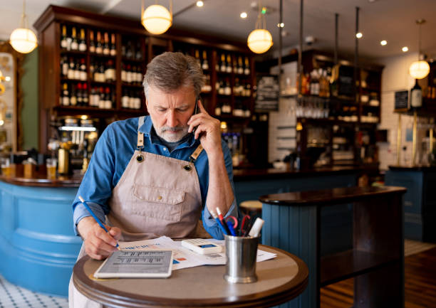 Business owner talking on the phone while working on the accountancy at a restaurant - Small business concepts